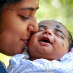 Heartwarming portrait of a mother kissing her smiling baby outdoors.