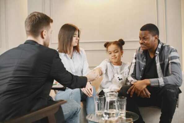 A family in a thoughtful counselling session with a professional in a modern setting.