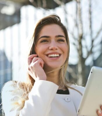 Confident businesswoman using her tablet and phone, smiling outdoors in sunlight.