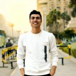 Smiling young man posing confidently on a city street during the day.